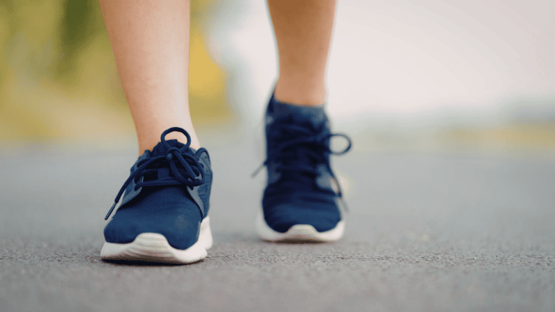 A first-person perspective of a beginner runner lacing up bright-colored daily training sneakers on a suburban paved path during a sunrise run.