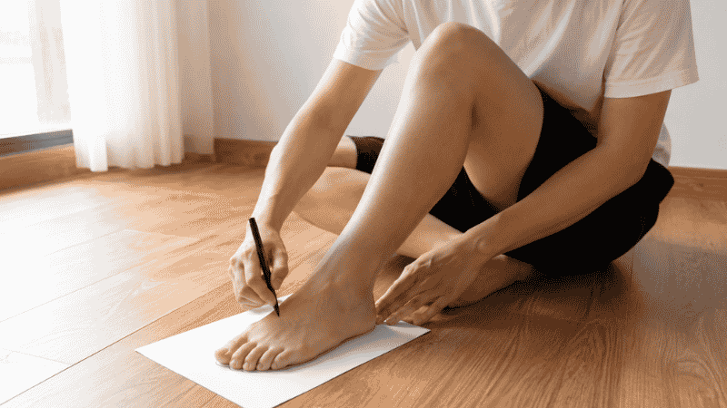 Person tracing their foot on white paper with a pen to measure foot size at home