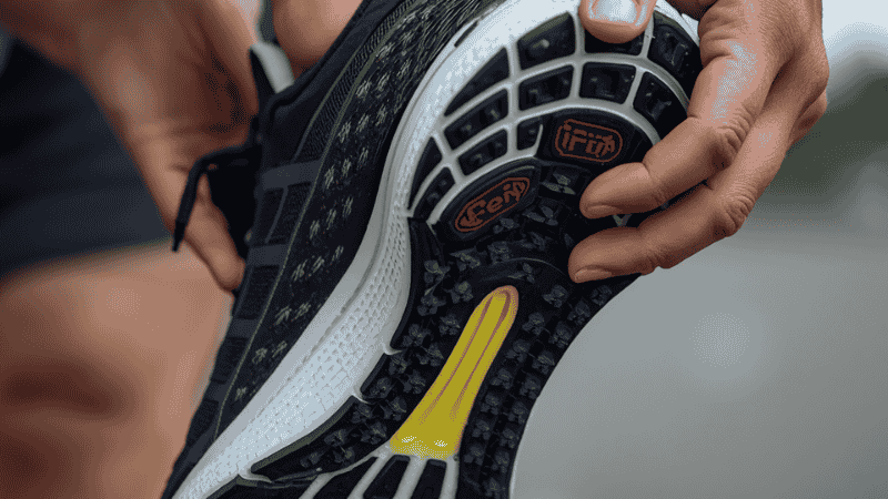 A close-up shot of a footwear reviewer demonstrating torsional rigidity by twisting the midsole of a running shoe to show arch support and flex points.
