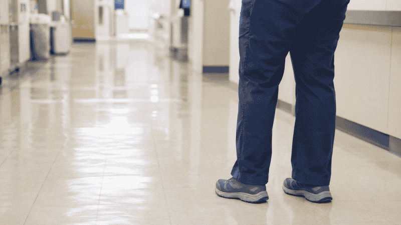 Nurse or healthcare worker standing on a hospital floor looking down at their work shoes after a long shift