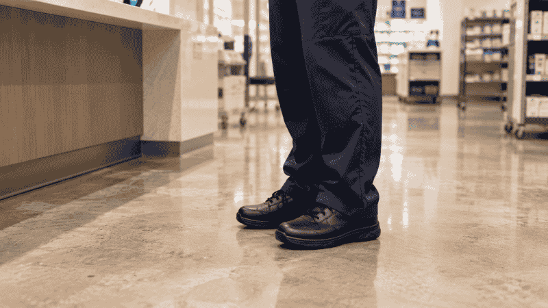 Healthcare worker or retail employee standing on a hard concrete floor in work shoes, representing the common scenario of ball of foot pain from prolonged standing