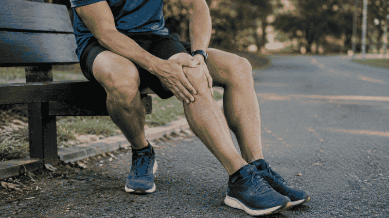 Runner sitting on a park bench holding their knee in pain after a run, representing the common experience of knee pain after running