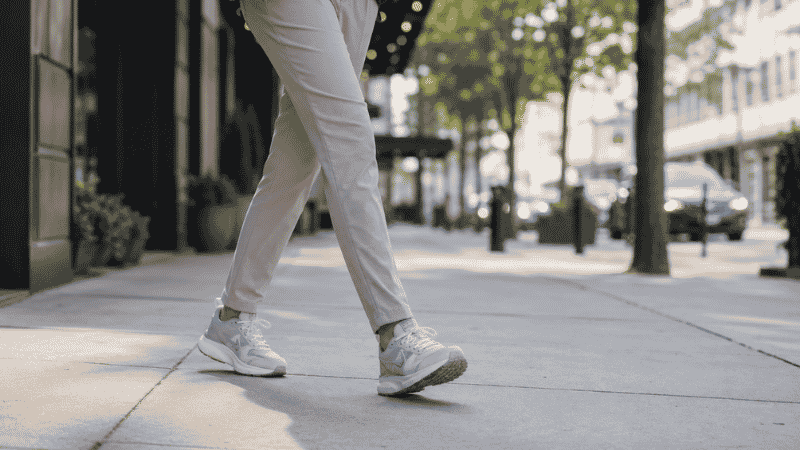 Person walking on a city street in well-fitted walking shoes, shown from the waist down, representing everyday walking shoe use for commuting and daily life