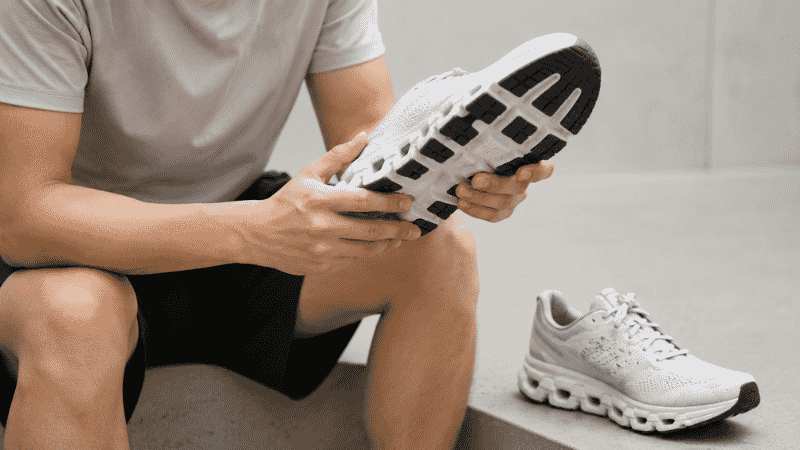 A runner examining the sole of a worn running shoe, comparing it to a new pair, showing the difference between a fresh midsole and a compressed worn-out midsole