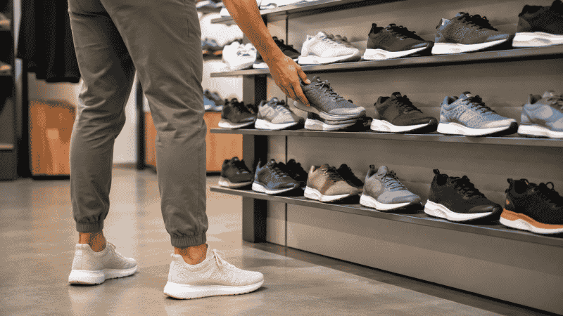 A runner examining multiple pairs of running shoes displayed on a shelf, representing the process of choosing the right running shoe based on foot type and running needs