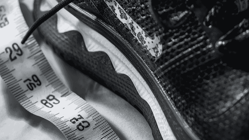 A close-up shot of the size label on the tongue of a pair of high-performance running shoes, juxtaposing the EU size 39 with a measurement in centimeters taken with a tape measure, serving to illustrate the actual length of a size 39 in women's footwear.
