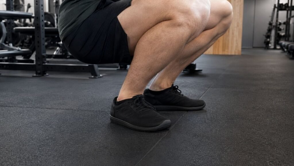 A person with flat feet performing a squat in a gym, showing the ankle alignment challenge that flat-footed gym-goers face when choosing the right training shoe